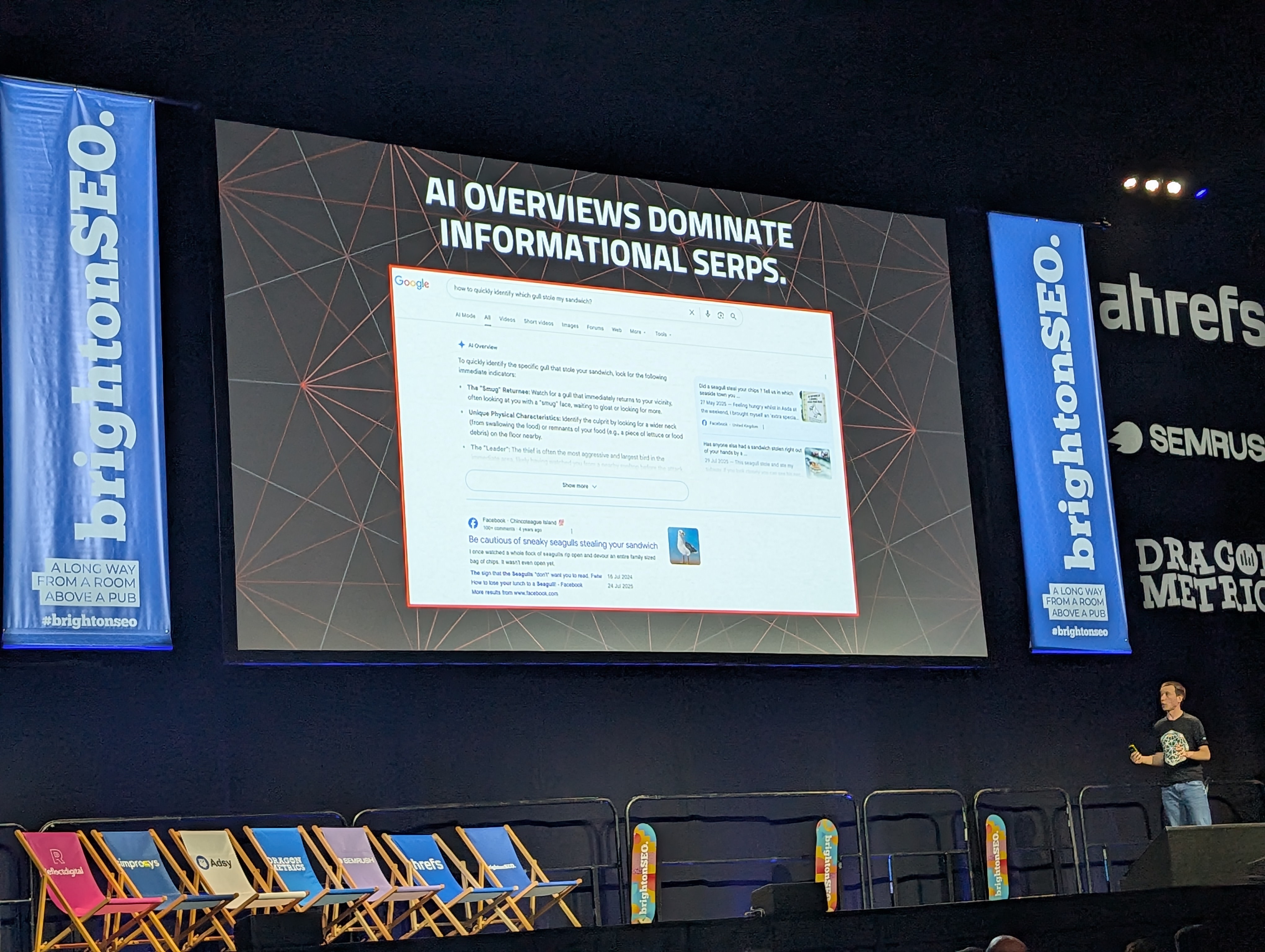 Tom Capper of Stat presenting at brightonSEO April 2026, slide reading AI Overviews Dominate Informational SERPs, showing a Google results page where an AI Overview fills most of the visible screen
